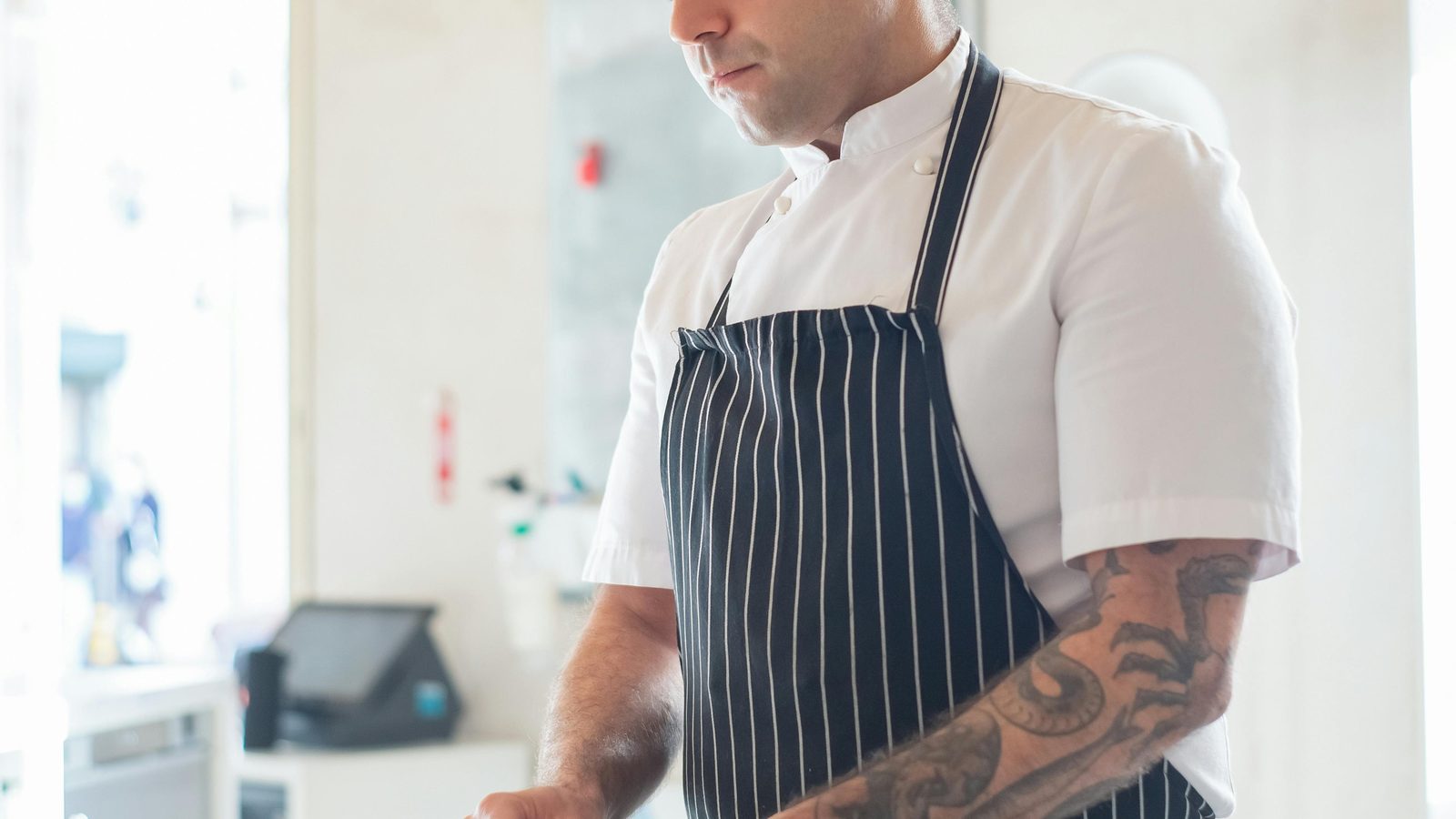A chef in whites and a striped apron working at the prep bench